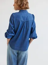 Camisa de denim azul con cuello mao con volados, mangas largas abullonadas con puños elásticos y cierre frontal con botones. Corte semi entallado.