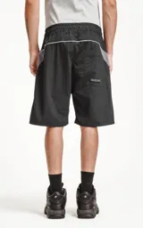 Bermuda negra de textil liviano con calce oversize, elástico y cordón de ajuste en la cintura. Presenta recortes con ribetes reflectantes grises en los bolsillos delanteros y ribetes blancos en el ruedo. Posee bolsillos traseros.