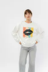 Buzo blanco de algodón rústico, con cuello redondo y terminaciones en rib. Estampa frontal multicolor con diseño de labios negros.