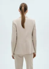 Blazer color beige con solapas de muesca, cierre frontal con un botón, hombros estructurados, corte entallado, forro interior y dos bolsillos de ribete en la parte delantera.