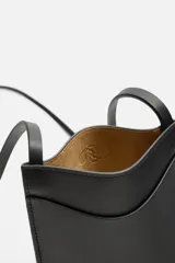 Bolso bandolera negro de cuero con bolsillo plano frontal y correa fina al hombro.