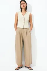 Pantalón color beige de corte holgado con silueta baggy. Modelo de tiro alto con pinzas, elástico revestido en la cintura, cierre y pretina prolongada con botón y corchete ocultos. Bolsillos al bies y bolsillos decorativos atrás.