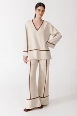 Pantalón de vestir color manteca, de corte recto y tiro alto, con detalle de ribetes marrones en los laterales.