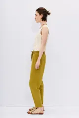 Pantalón babucha de tiro alto confeccionado en símil lino color verde oliva. Tiene calce relajado que ajusta hacia el ruedo y largo hasta los tobillos, cintura elastizada con lazo de ajuste, bolsillos diagonales en laterales y dos bolsillos ojal falsos en espalda.