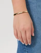 Pulsera rígida dorada tipo brazalete con dije de corazón.