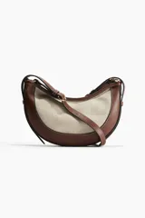 Cartera marrón con panel frontal de lona color crema, forma de media luna y correa ajustable.