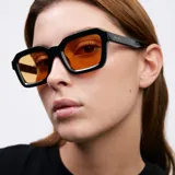 Lentes de sol con armazón cuadrado de color negro y bordes gruesos, inspirados en la moda de los años 70. Poseen cristales de color naranja con protección UV400.
