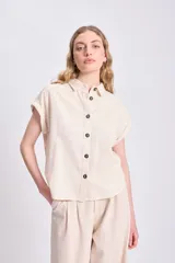 Camisa color crudo de lino, con cuello clásico, manga corta con dobladillo y cierre frontal con botones negros.