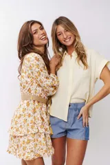 Vestido corto con estampado floral amarillo y blanco, mangas largas abullonadas y falda con volados. Incluye cinturón de soga.