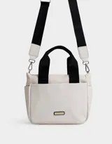 Cartera tipo tote color blanco hueso, con doble asa corta negra y correa larga negra regulable y desmontable. Tiene cierre superior, bolsillos laterales y tag de goma con el logo de la marca.