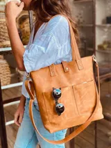 Bolso tipo tote bag color suela, de cuero, con doble asa de mano y correa larga extraíble y ajustable. Tiene dos bolsillos externos grandes.