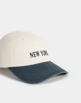 Gorra de béisbol bicolor, con la parte superior color crema y la visera azul denim. Tiene bordada la frase "New York" en azul marino.