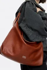 Bolso de mano negro con exterior de piel y estructura blanda. Incluye asa extraíble, bolsillo interior y etiqueta de tejido. Presenta logo metálico BIMBA Y LOLA con acabados metálicos plateados.