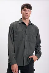 Camisa de hombre color verde oscuro de pana con cuello clásico, cierre frontal con botones, dos bolsillos de parche en el pecho y mangas largas con puños abotonados.