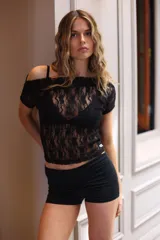 Top negro de manga corta con escote Bardot (hombros descubiertos), confeccionado en encaje floral transparente.