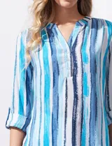 Blusa de gasa estampada con rayas verticales en tonos celeste, azul y blanco. Tiene cuello a la base con escote en V y abertura con botones. Las mangas largas son de largo regulable.
