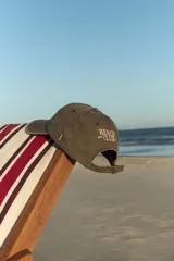 Gorra de gabardina color verde oliva con bordado frontal "Beach Club" en color rojo y detalle de etiqueta roja en el lateral.