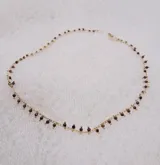 Collar dorado con cadena fina y pequeños colgantes negros.
