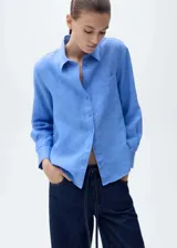 Camisa celeste de lino con cuello camisero, manga larga con puños abotonados, cierre frontal con botones, bolsillo de parche en el pecho y corte recto.