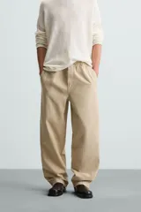Pantalón de algodón color beige con efecto lavado, corte relajado y pierna ancha. Presenta cintura elástica con ajuste de cordón y cierre frontal con botón, además de bolsillos delanteros y bolsillos traseros de plastrón.