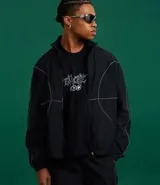 Campera deportiva negra con cuello alto, cierre frontal de cremallera y elásticos en puños y bajo. Presenta recortes geométricos definidos por costuras en hilo reflectante.