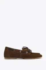 Zapato náutico color marrón de serraje con detalle de pespuntes en el cuerpo y pasados en los laterales. Cierre mediante cordones y suela efecto engomado.