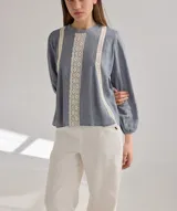Camisa celeste de algodón con detalle de encaje blanco en el frente. Tiene mangas largas abullonadas con puños anchos y cuello redondo.