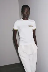 Camiseta blanca de corte slim fit, cuello redondo y manga corta. Detalle de acabados en tricot con hilo metalizado color dorado en mangas y bolsillo.