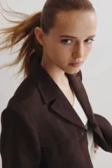 Blazer marrón oscuro con solapas de muesca, dos botones frontales y dos bolsillos de parche grandes en la parte inferior. Presenta canesú delantero y trasero y hombreras.