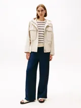 Campera beige de Tommy Hilfiger, con capucha con cordón ajustable y cierre frontal con cremallera y botones a presión. Tiene dos bolsillos delanteros tipo sobre con botón y logo metálico de Tommy Hilfiger en el puño.