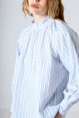 Blusa celeste con rayas verticales blancas, cuello mao y mangas largas abullonadas con puños elásticos.