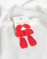 Aros colgantes de acrílico rojo con piezas geométricas irregulares unidas por argollas doradas.