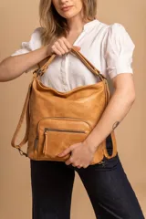 Cartera mochila color tostado, símil cuero, con compartimiento principal amplio y bolsillos frontales con cierre. Tiene correas ajustables para usar como mochila y asa superior para llevar al hombro.