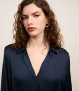 Camisa blanca de satén con cuello inglés, manga larga y cierre frontal con botones.