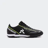 Championes de fútbol Le Coq Sportif modelo Magic Match, color negro con detalles en amarillo flúor y blanco. Presentan el logo del gallo en blanco y la inscripción "le coq sportif" en amarillo flúor en el talón. Tienen suela de goma con tacos bajos, aptos para superficies de césped sintético o fútbol sala.