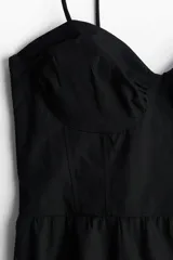 Vestido corto negro de popelina de algodón con breteles finos ajustables con moña, escote corazón y cuerpo entallado con costuras decorativas y espalda fruncida. Falda acampanada con costura fruncida en el bajo.