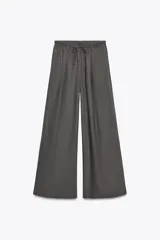 Pantalón blanco de lino, de corte ancho y tiro medio, con cintura elástica ajustable con cordones y bolsillos laterales.