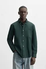 Camisa azul marino de corte regular fit, confeccionada en tejido de algodón Oxford. Tiene cuello abotonado, manga larga con puños abotonados, bolsillo de parche en el pecho y cierre frontal con botones.