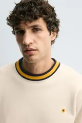 Sudadera color crema de corte regular fit, cuello redondo y manga larga. Presenta ribete a rayas en cuello, puños y bajo. Tiene un pequeño bordado de una flor en el pecho.