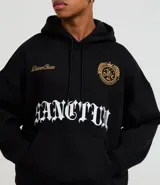 Hoodie negro de corte boxy, con capucha ajustable, bolsillo canguro y detalles bordados en el pecho. Presenta un estampado grande en la parte frontal con tipografía gótica y texto en dorado.
