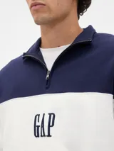 Buzo de algodón color azul marino con diseño de bloques de color, presentando una franja horizontal blanca en el pecho con el logo "GAP" estampado en azul oscuro. Tiene cuello alto con cierre parcial (medio cierre) y puños y cintura acanalados.