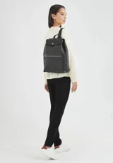 Mochila de cuero color negro con cierre de solapa con botón a presión y bolsillo frontal con cierre de cremallera.