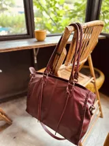 Bolso tipo tote de cuero color borgoña con doble asa de hombro, correa bandolera ajustable y detalles de costuras a la vista.
