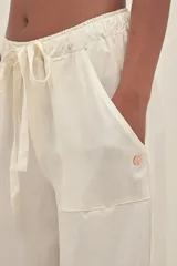 Pantalón color crema de lino y tencel, con bolsillos laterales, cintura elástica y cordón ajustable. Detalle regulable en el tobillo.