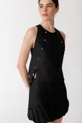 Musculosa negra de lino con cuello redondo, sin mangas y abertura lateral. Presenta detalles de tachas doradas en los hombros y en la abertura lateral.
