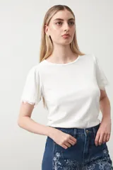 Remera de tejido acanalado color blanco, con cuello redondo y mangas cortas que presentan un detalle de terminación en puntilla en los bordes.