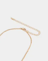 Collar corto dorado con cadena de eslabones y dijes colgantes en forma de corazón con incrustaciones de cristal.