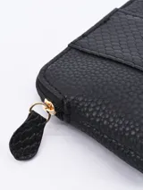 Monedero negro con textura símil piel de reptil y cierre superior con cremallera dorada.