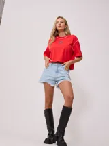 Remera gris de algodón con corte cropped y calce holgado. Tiene cuello redondo y mangas cortas con costuras reforzadas en color coral. Presenta un pequeño logo de la marca Rusty en el pecho.