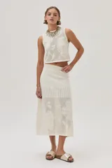 Falda midi color crudo, tejida de punto calado con diseño de flores. Cuenta con elástico y lurex en la cintura.